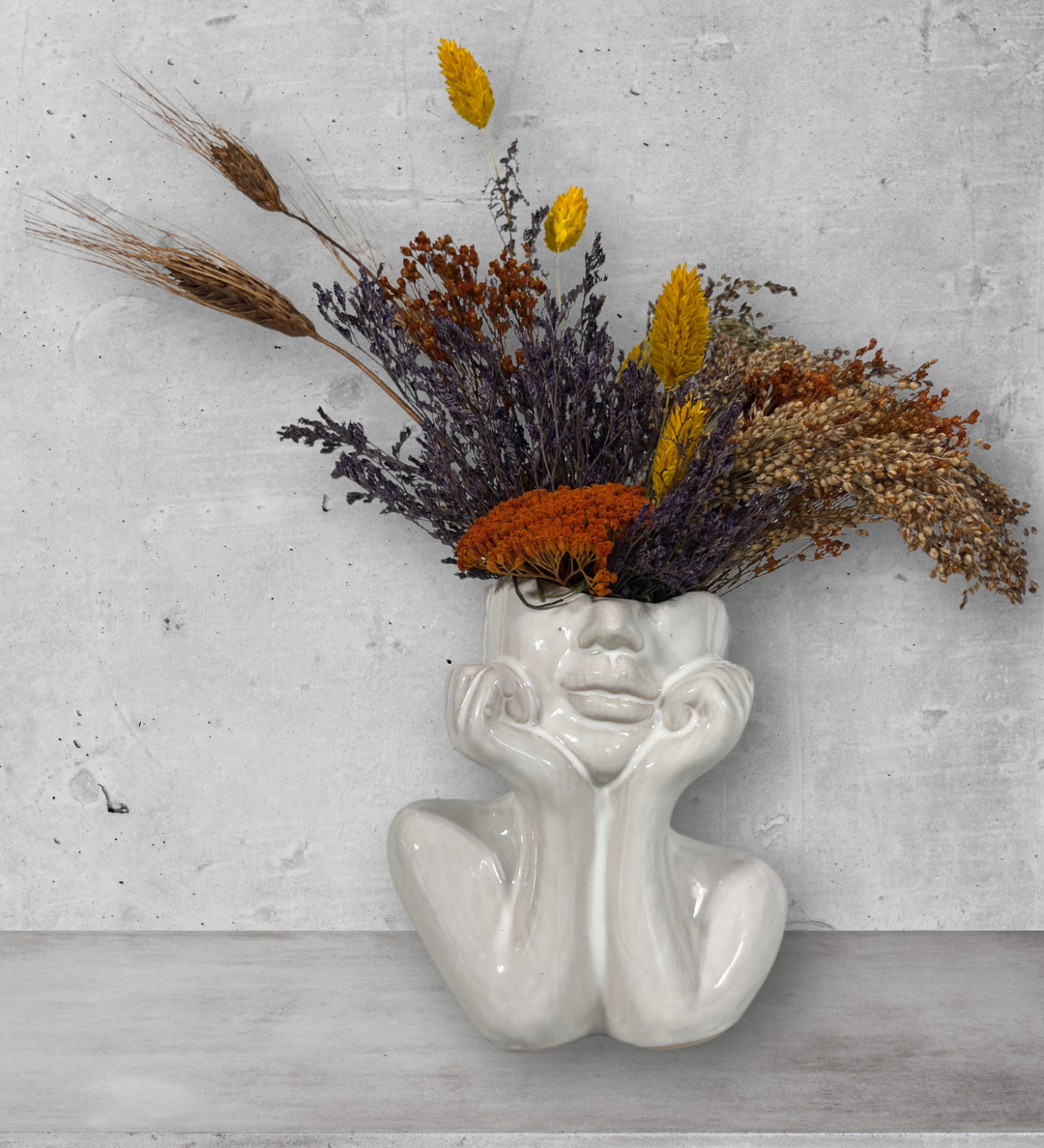 Decorative vase shaped like a face with dried flowers on a gray surface