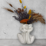 Decorative vase shaped like a face with dried flowers on a gray surface